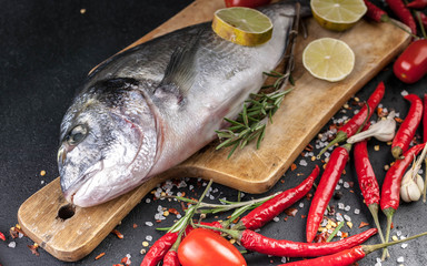 Fresh Dorado on a wooden cutting board. Aromatic herbs, lime, cherry tomatoes, salt, paprika and spices. Close-Up