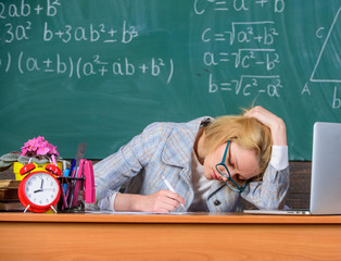 Wall Mural - Teacher woman sit table classroom chalkboard background. Still working. Work far beyond actual school day. Teacher tired face keep working after classes. Teacher busy with paperwork and research