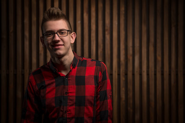 Wall Mural - The guy in the plaid shirt. Guy in the interior. Young handsome guy. Man standing near the wooden walls.