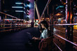 © LIGHTFIELD STUDIOS - side view of young woman using laptop on street with night city lights on background