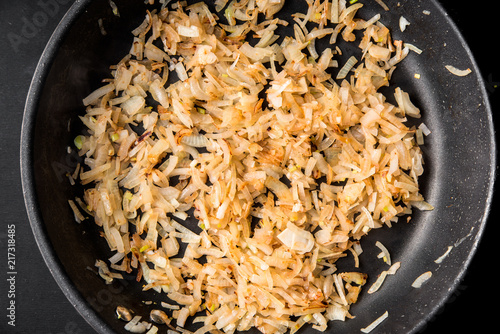 Fotografie, Obraz Sliced onions are fried in a frying pan, top view