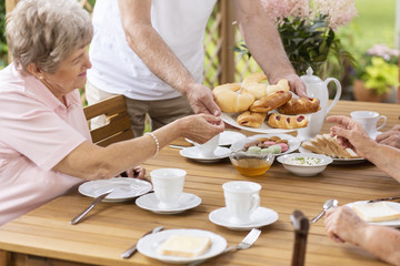 Wall Mural - Person sharing food with elderly woman during breakfast in the terrace