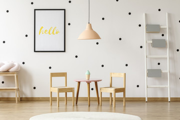 Wall Mural - Pastel pink pendant above wooden play dining set for kids and books on a ladder in a cute preschool room interior with black and white polka dot wallpaper