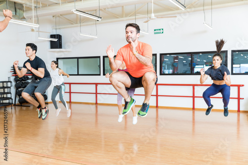 Fotografie, Obraz Clients Doing Tuck Jumps On Hardwood Floor In Gym