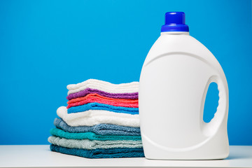 Wall Mural - Photo of one white bottle of cleaning agent and stack of multi-colored towels isolated on blue background