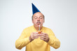 Mature man in birthday cap blowing candle on his cake making a wish.
