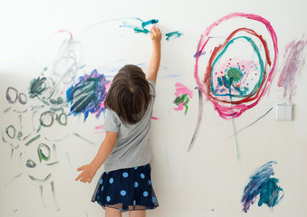 Curly cute little toddler girl painting with paints color and brush on the wall. Works of child