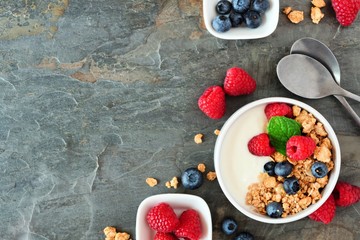 Wall Mural - Healthy yogurt with raspberries, blueberries and granola. Above view, corner border over a dark background. Copy space.