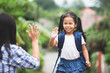 © pingpao - Back to school. Cute asian child girl with school bag and her mother making hi five gesture before go to school with fun