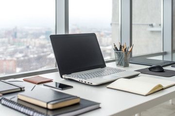 Workplace with notebook laptop Comfortable work table in office windows and city view.