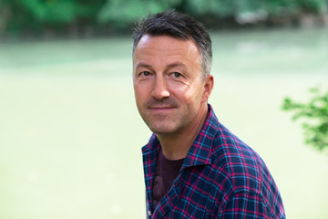 Man' s outdoor portrait. Handsome mature man lokking at camera and smiling over nature background.