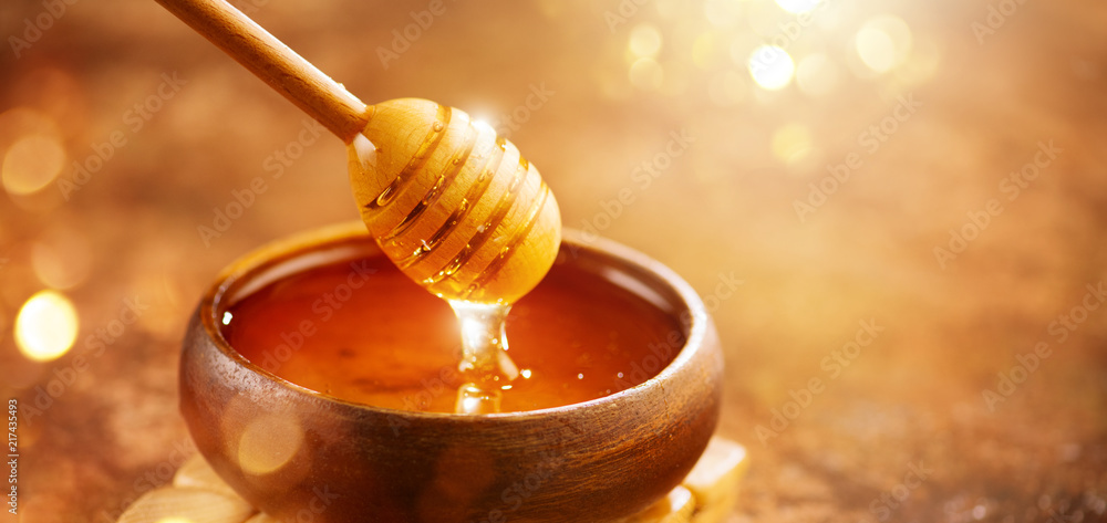 Honey. Healthy organic thick honey dripping from the honey dipper in wooden bowl. Sweet dessert background - obrazy, fototapety, plakaty 