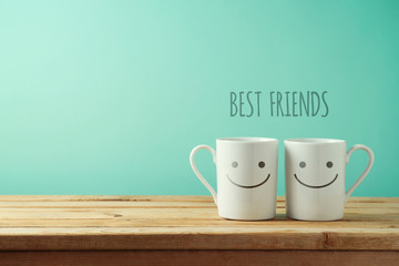 Wall Mural - Coffee cups with funny faces on wooden table