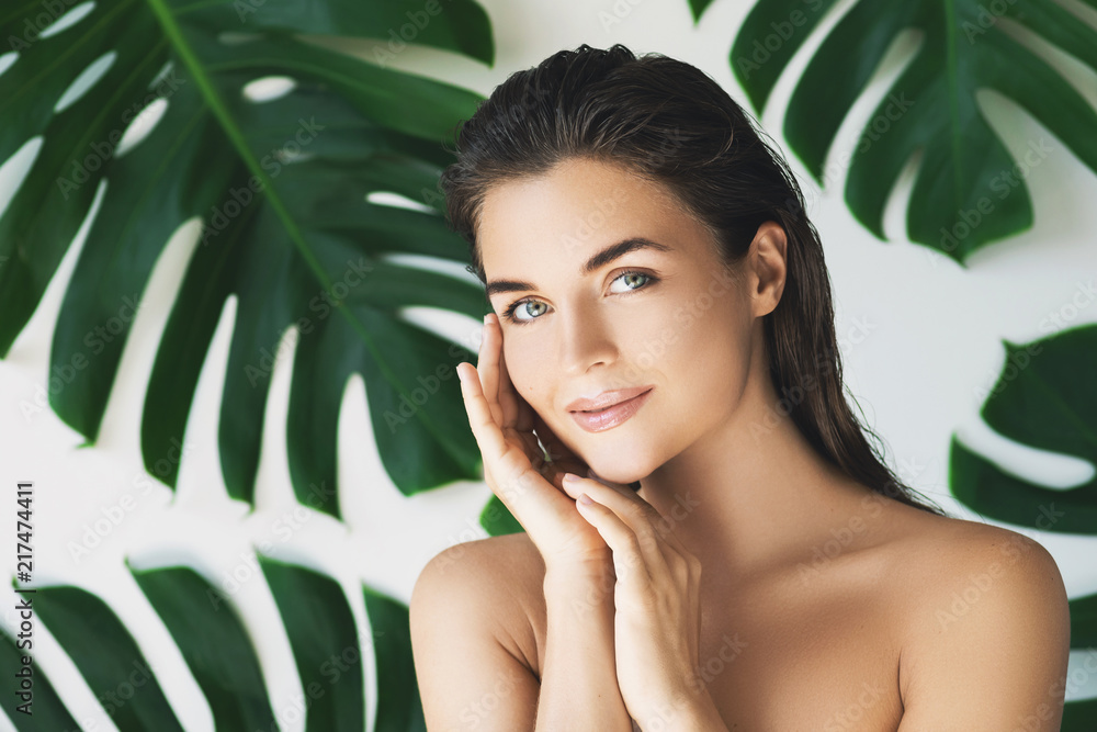 Portrait of young and beautiful woman with perfect smooth skin in tropical leaves - obrazy, fototapety, plakaty 