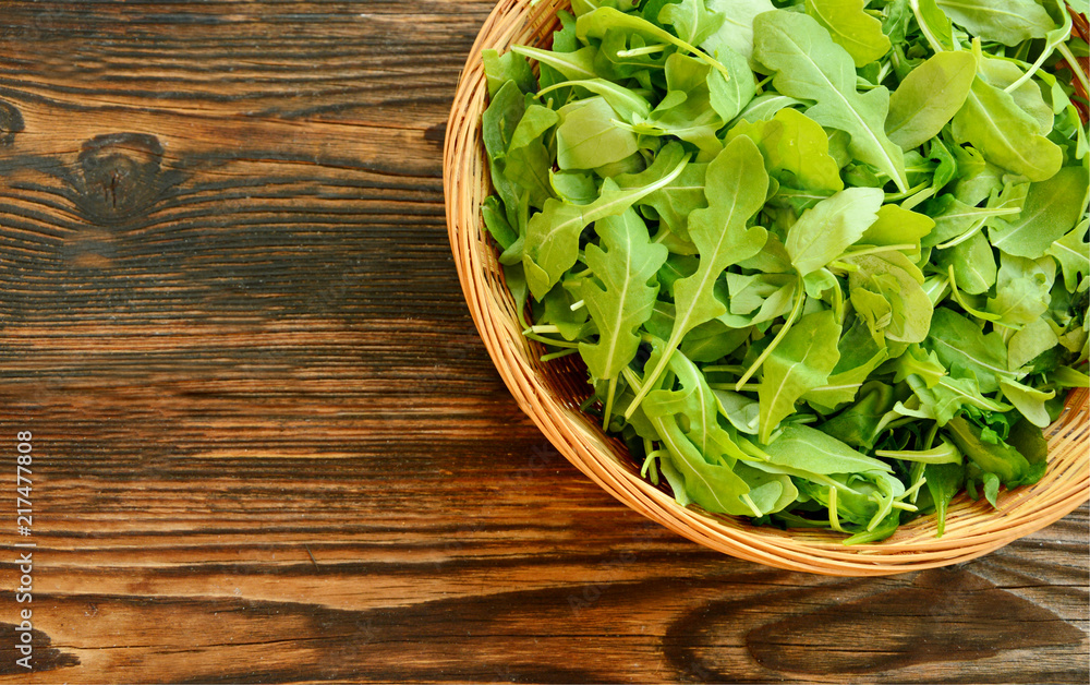 Arugula, rocket and rucola in the basket on wooden floor. The presence ...