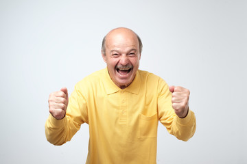 mature hispanic man in yellow shirt celebrating victory of his team over gray background.