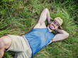 © starsstudio - Attractive, fit young man relaxing laying down in a grass field, wearing straw hat, looking at camera, smiling