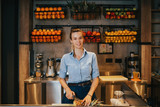 Happy young female bartender standing at juice bar counter and working.