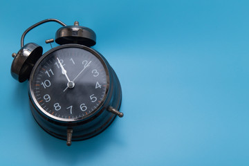 Black vintage alarm clock on blue background.