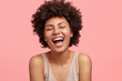 Leinwandbild Motiv Joyful African American female with dark skin, laughs happily, opens mouth widely, has sparkles on cheeks, closes eyes, has curly hair, isolated over pink background. People and happiness concept