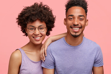 Wall Mural - Horizontal shot of happy African American woman and man have truthful relationships, toothy smile, happy to meet with friends, dressed casually, isolated over pink background. Emotions concept