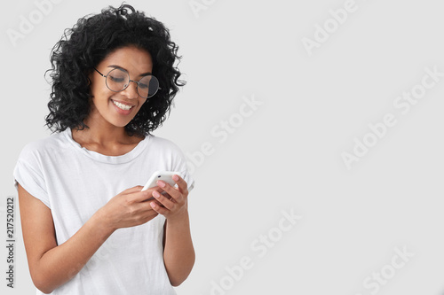 Fotografía Cheerful African American with crisp hair, holds modern smart phone, happy to re