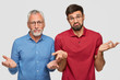 © WHstudio Leushin N - Indoor shot of puzzled mature male and his adult son, shrugg shoulders, can`t make decision, being unshaven, stand closely to each other against white background. So what to do in this situation?