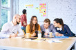 © baranq - Team of young startup businesspeople looking at tablet during brainstorming session. Cheerful university students studying together