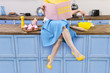 © Monstar Studio - Colorful retro / pin up girl woman female housewife wearing yellow top, skirt and white apron sitting on kitchen and reading pink cook book. Sweet food cupcakes and milkshake home cooked on the table