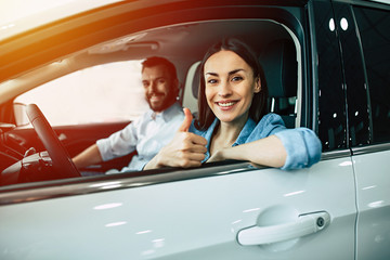 Wall Mural - Happy beautiful young couple chooses and buying a new car for the family in the dealership while sitting inside one of car.