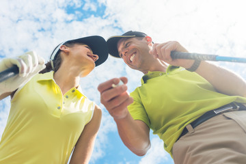 Low-angle view portrait of a young woman smiling while looking at camera during professional golf game with her partner or instructor outdoors