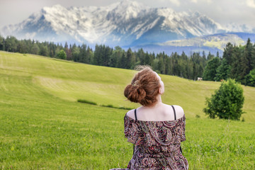 Wall Mural - Young woman sitting on grass, alpine landscape.