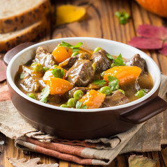  Beef stew with pumpkin, peas and thick sauce, autumn food. Dark bowl on wooden background in rustic style