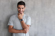 © Damir Khabirov - Portrait of handsome man in t shirt, standing against gray textured wall with copy space for your ads, showing his stylish modern smart watch with empty screen