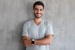 © Damir Khabirov - Portrait of smiling handsome man in t shirt and smart watches, standing with crossed arms against gray textured wall