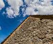 Close up detail of a medieval stone wall and roof top with a blue sky and clouds in the background, Cotswolds, England