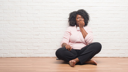 Canvas Print - Young african american woman sitting on the floor wearing headphones looking stressed and nervous with hands on mouth biting nails. Anxiety problem.