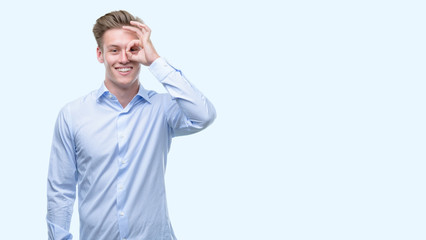 Poster - Young handsome blond man with happy face smiling doing ok sign with hand on eye looking through fingers