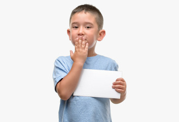 Canvas Print - Dark haired little child holding a blank card cover mouth with hand shocked with shame for mistake, expression of fear, scared in silence, secret concept