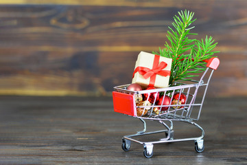 Wall Mural - Christmas shopping concept. Shopping cart, Christmas gift and decoration on wooden background with copy space