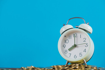 Vintage alarm clock on the pile of gold coin with blue background, time and business finance concept.