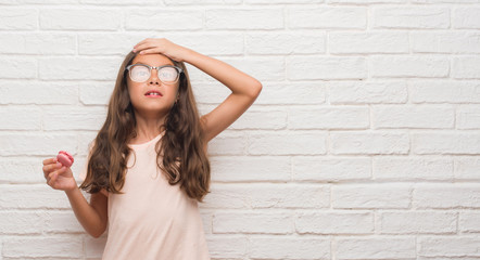 Poster - Young hispanic kid over white brick wall eating pink macaron stressed with hand on head, shocked with shame and surprise face, angry and frustrated. Fear and upset for mistake.