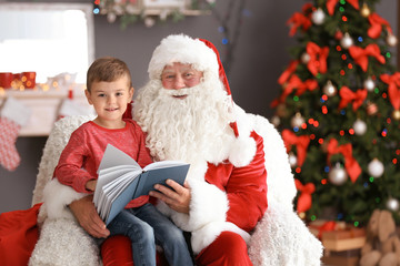 Canvas Print - Little boy reading book while sitting on authentic Santa Claus' lap indoors