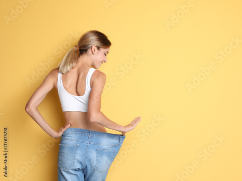 Photographie Young slim woman in old big jeans showing her diet results on color background