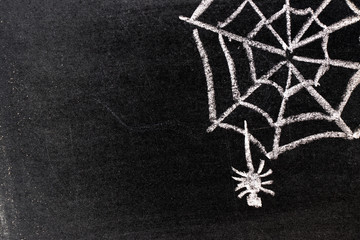 white chalk hand drawing in cobweb with spider shape on blackboard background