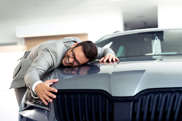 Wall Mural - Portrait of a businessman smiling joyfully and embracing a new car at the dealership showroom