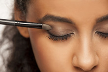 Portrait Of A Young Dark-skinned Woman Applying Eye Shadow With Brush On A White Background
