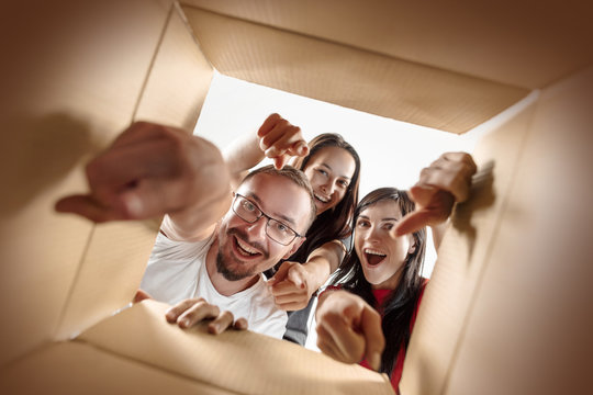 The surprised caucasian man and women opening carton box and looking inside. The package, delivery, surprise, gift, lifestyle concept. The smiling people pointing to camera