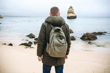 Wall Mural - A tourist or traveler with a backpack walks along the coast of the Atlantic Ocean and admires the beautiful view of the ocean near the city called Lagos in Portugal.