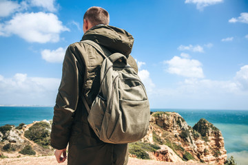 Wall Mural - A tourist or traveler with a backpack walks along the coast of the Atlantic Ocean and admires the beautiful view of the ocean near the city called Lagos in Portugal.